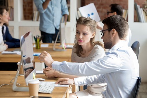 Executive manager mentor teaching intern employee giving instructions showing new online project pointing on computer screen, serious worker helping explain colleague listen work task look at monitor